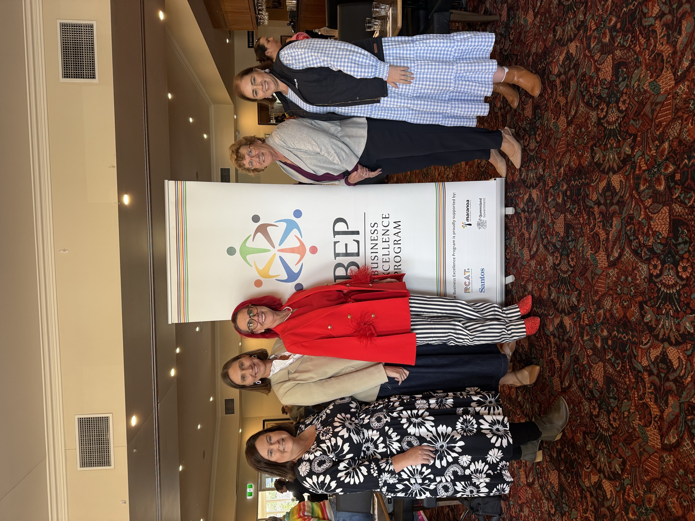 Tracy Sheen with the Business Excellence Program team in front of the BEP banner at the Roma Explorers Inn